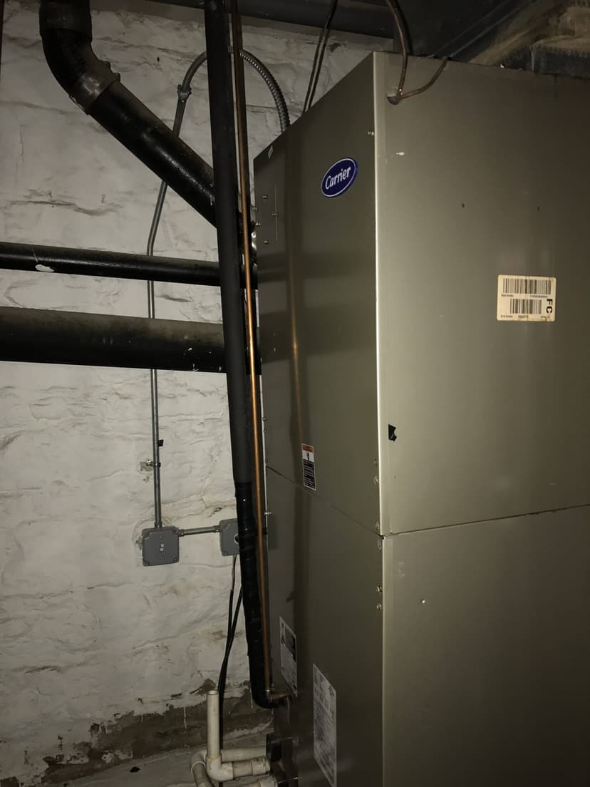 A Carrier HVAC unit, featuring an advanced air handler, is installed in a basement, surrounded by pipes and a concrete wall in the background.