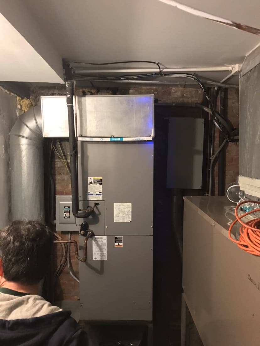 A technician inspects a large air handler in a dimly lit room, with pipes and ducts intricately connected to the HVAC equipment.