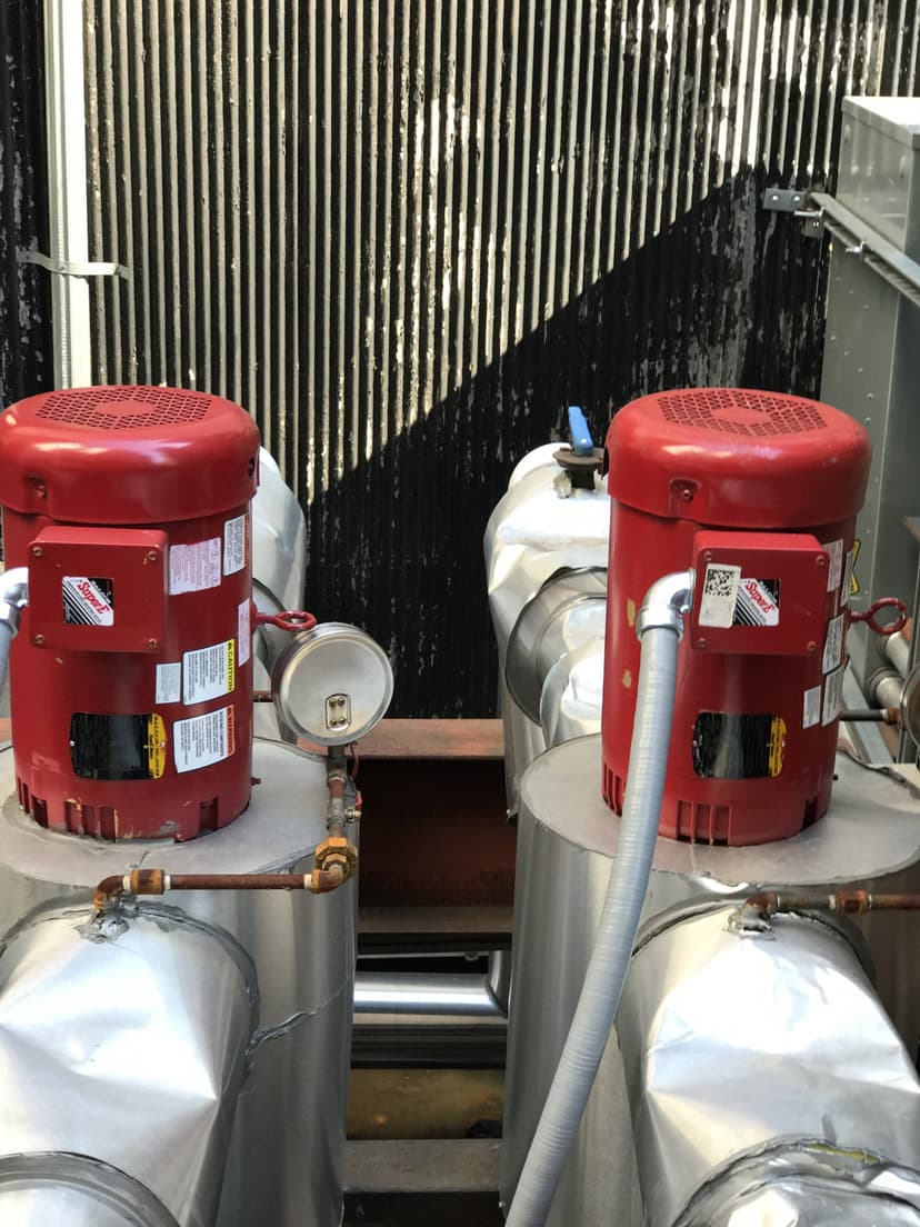 Two large red industrial motors connected to pipes, with gauges and labels, located in an industrial setting, power the centrifugal chiller pump system.