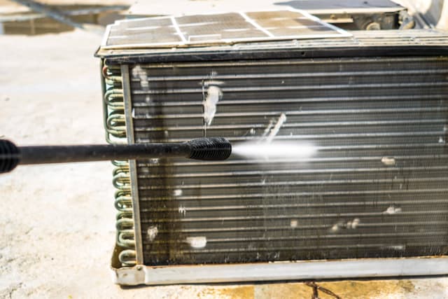 A man uses a hose to clean an air conditioner.