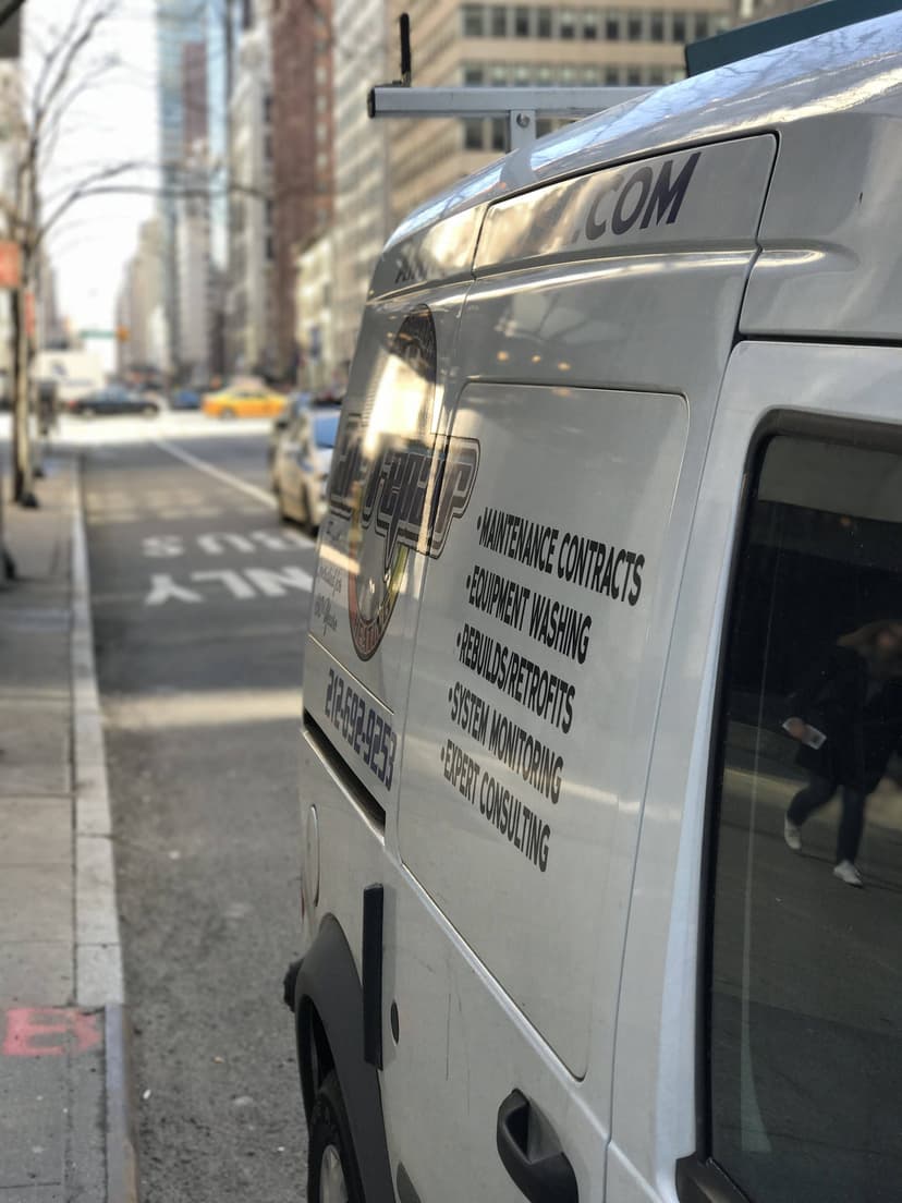 Side view of a parked white maintenance van with Air Repair Company branding and services listed on its side on a city street.