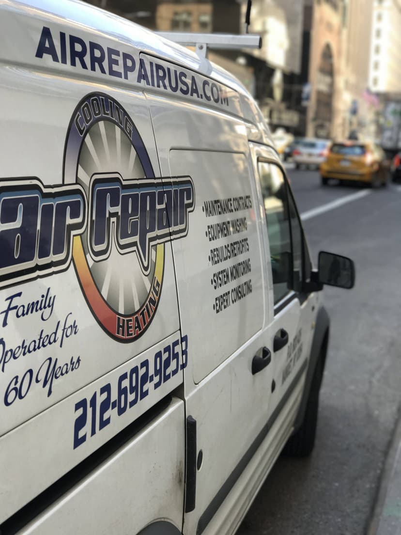 White van with 'Air Repair Company' branding and contact details parked on a city street. Taxi and buildings in the background.