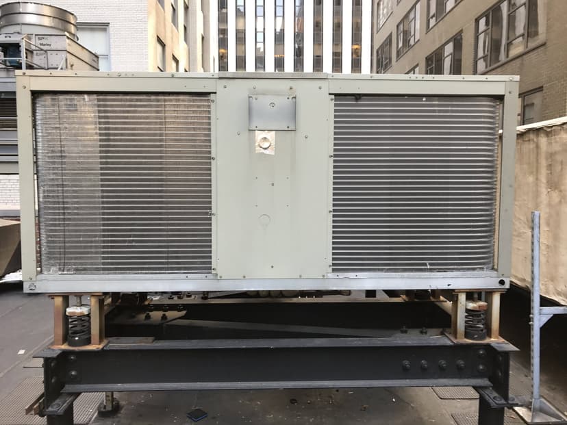 Large outdoor condensing units mounted on a platform, situated between tall buildings in an urban environment.