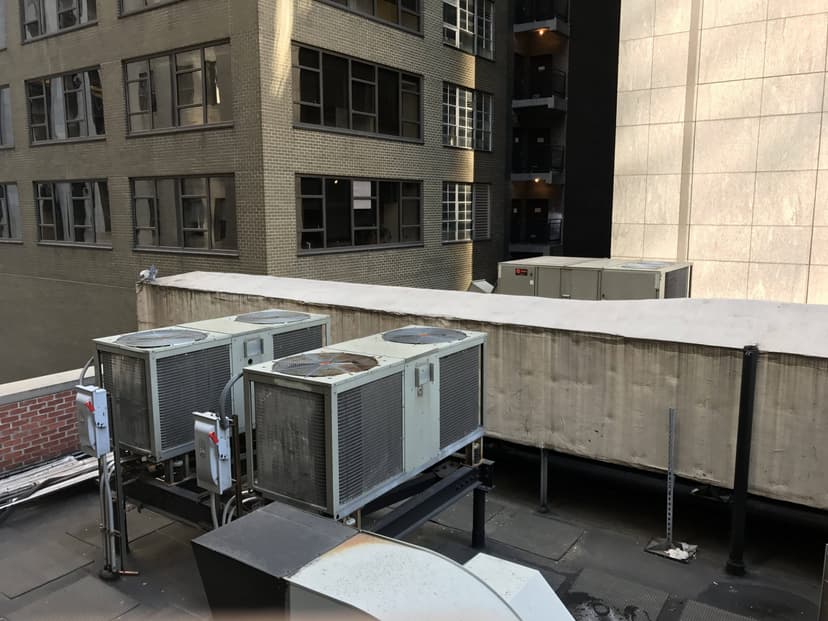 A view of several rooftop condensing units with a city building backdrop.