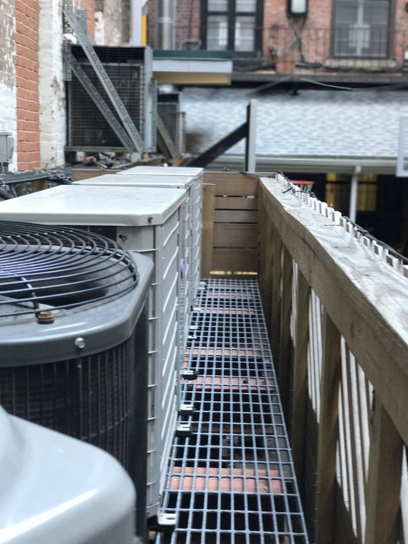 Outdoor air conditioning and condensing units, along with ventilation systems, sit on a metal platform beside a building with a wooden railing.