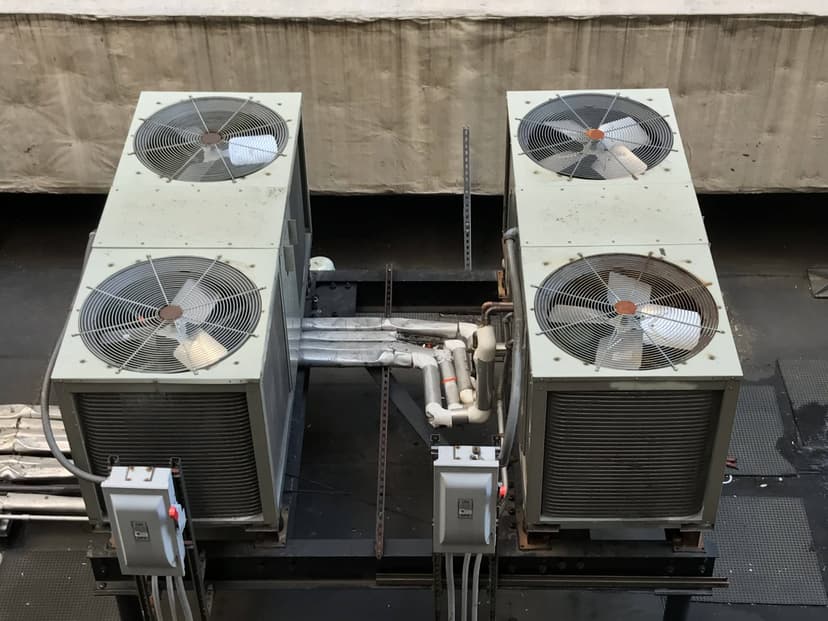 Four industrial air conditioning condensing units installed on a metal platform on a rooftop. Pipes and wiring are visible.