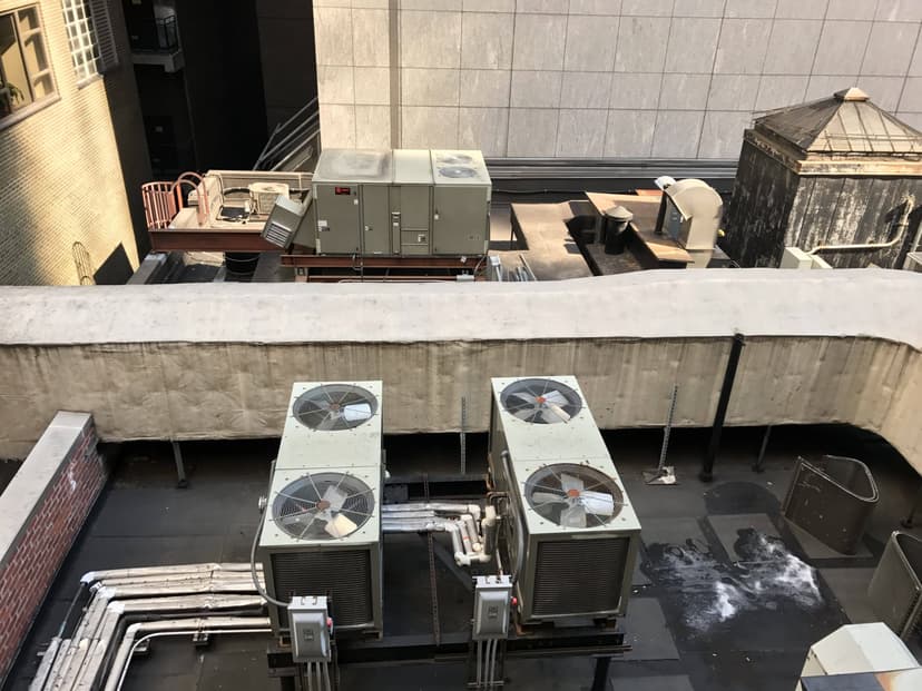 Rooftop view of multiple condensing units with ventilation ducts and a weathered building in the background.