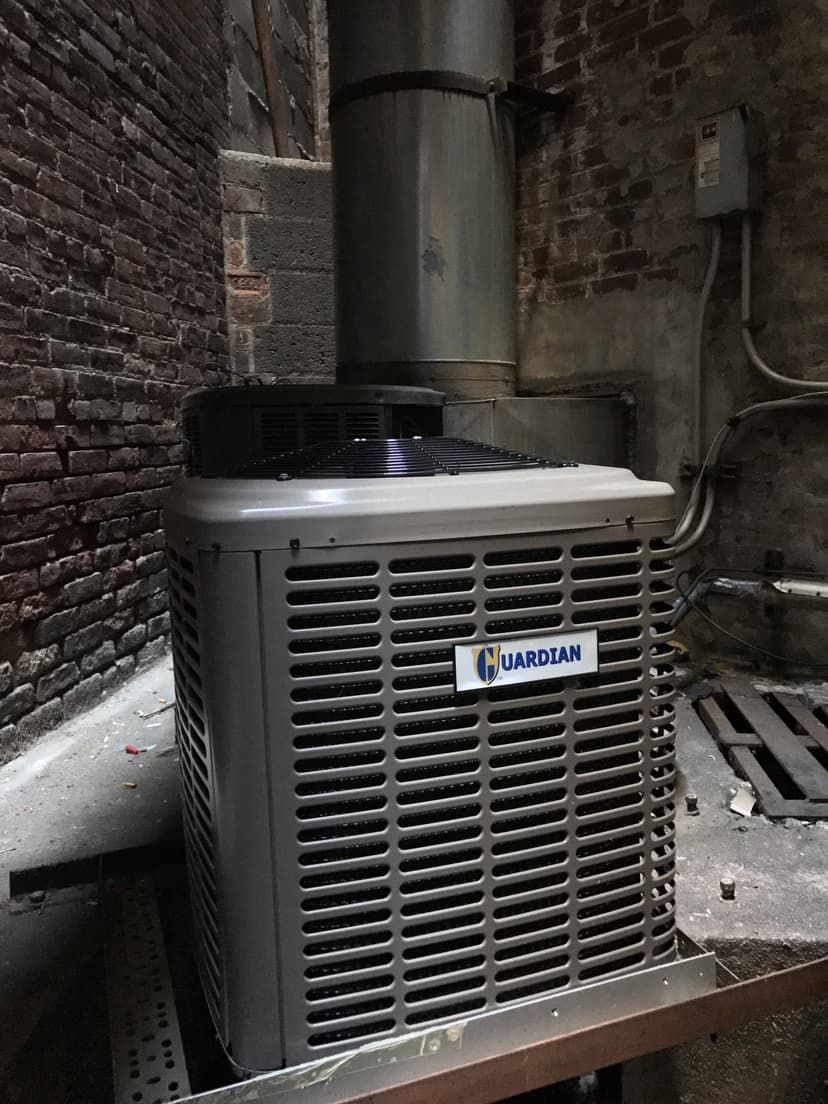 An outdoor Guardian HVAC condensing unit installed in a narrow brick alleyway.