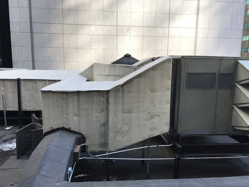 Large grey HVAC units on a rooftop, showcasing an exemplary setup of duct work against the backdrop of a tall building.