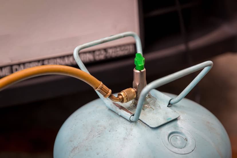 A close-up of an air conditioning refrigerant tank filled with Freon, featuring a connected hose and attached valve with a green cap.