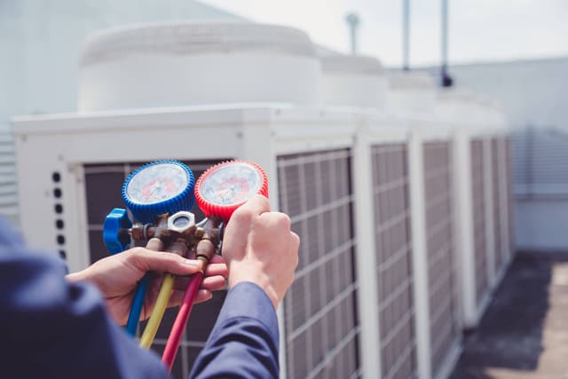 A man holding a gauge in front of an air conditioning unit.