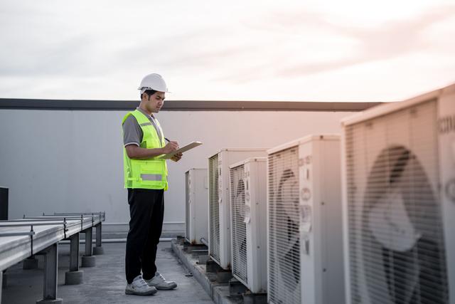 A man is standing on top of an air conditioning unit.