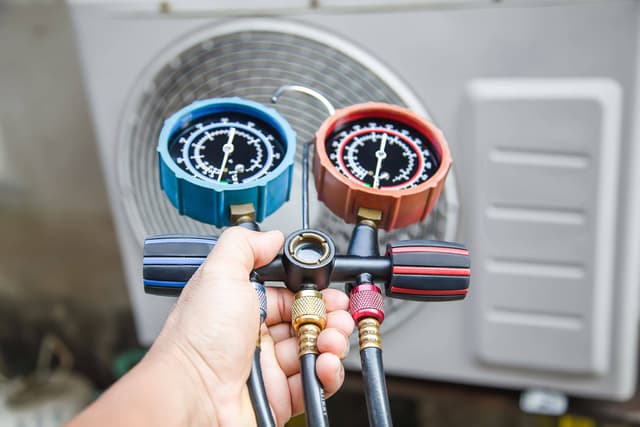 A person holding a gauge in front of an air conditioner.