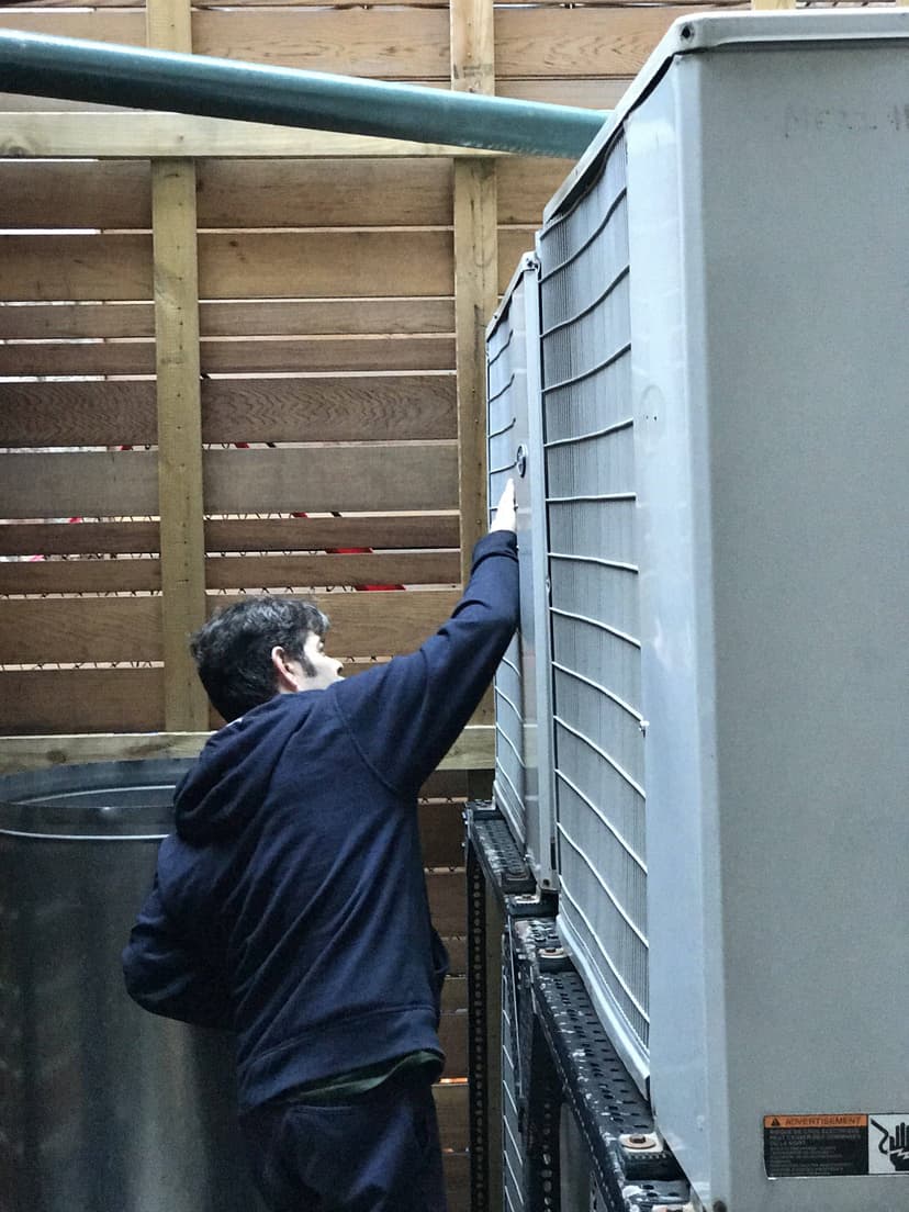 A person in a hoodie inspecting the control panel of a large air conditioning unit, embodying the expertise of HVAC mechanics in NYC's industrial settings.