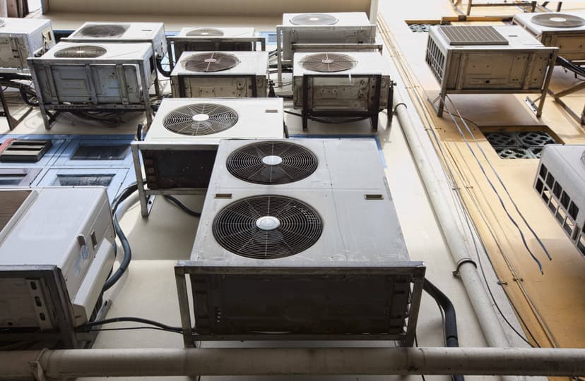 Multiple air conditioning units, part of a commercial HVAC system, are mounted on the exterior of a building with pipes and cables connected to each unit.