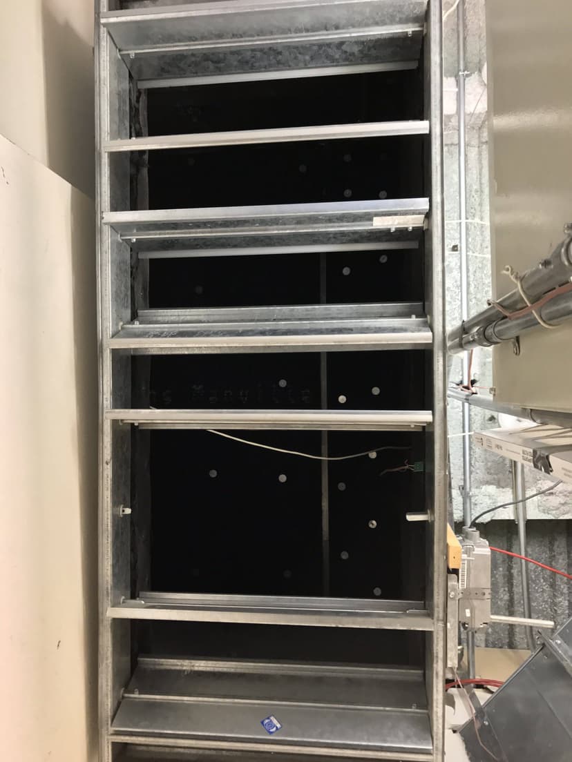 Metallic support structure with cables, conduits, and commercial HVAC equipment in a building under construction, viewed from below.