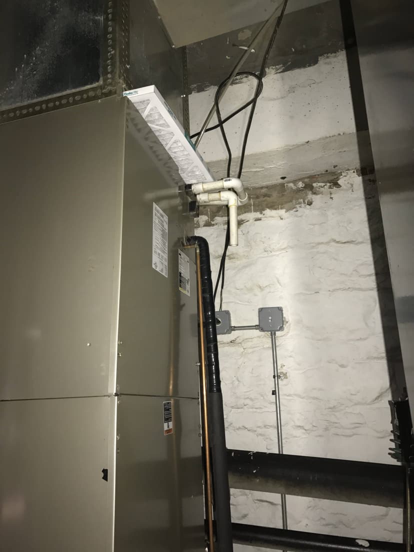 A commercial indoor HVAC unit sits in the basement, with visible pipes and electrical wiring weaving along the textured wall.