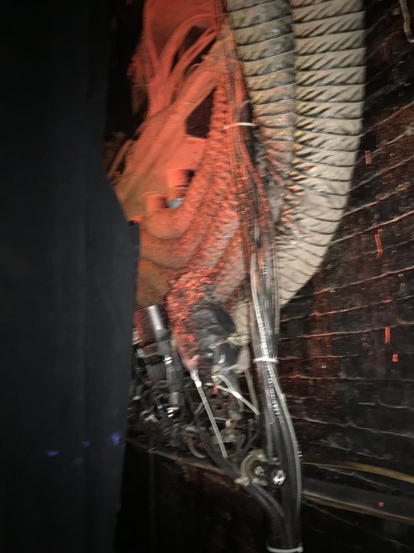 Tangled cables and wires with a backdrop of a black wall and some black fabric, illuminated by dim red light, create an industrial scene reminiscent of indoor commercial HVAC equipment.