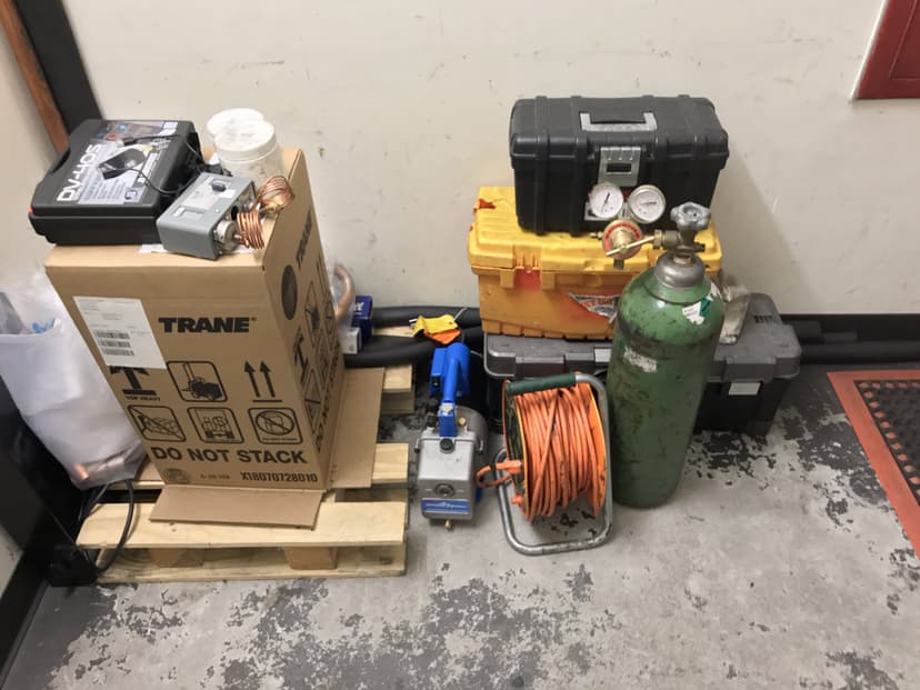 Pallet with various commercial HVAC equipment, including a green gas cylinder, coiled orange cable, toolboxes, and boxes labeled Trane.