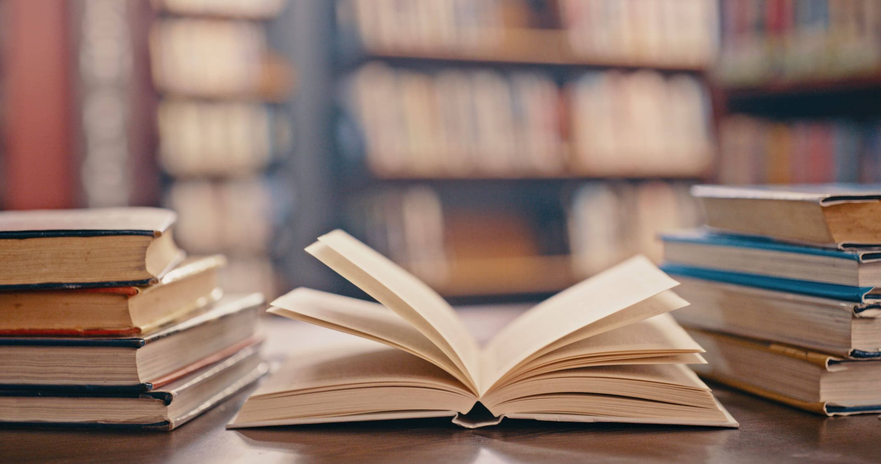 A stack of books on a table in front of a library.