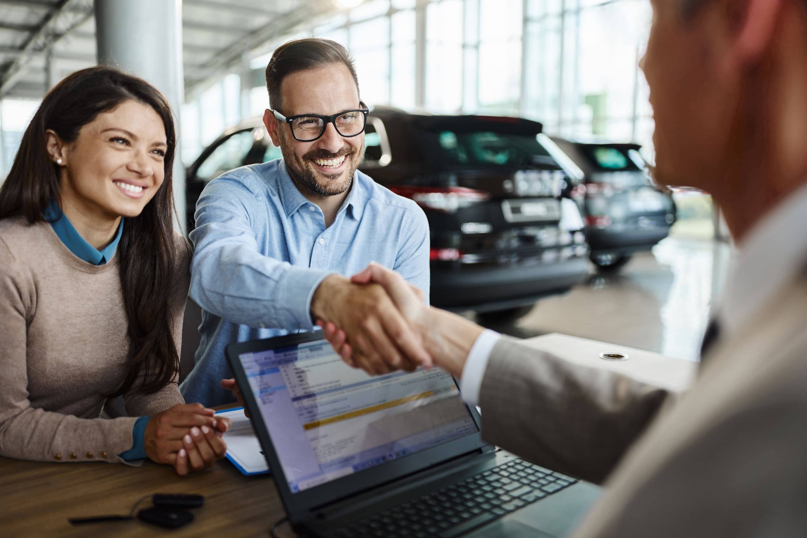 A man and woman shaking hands at a car dealership.