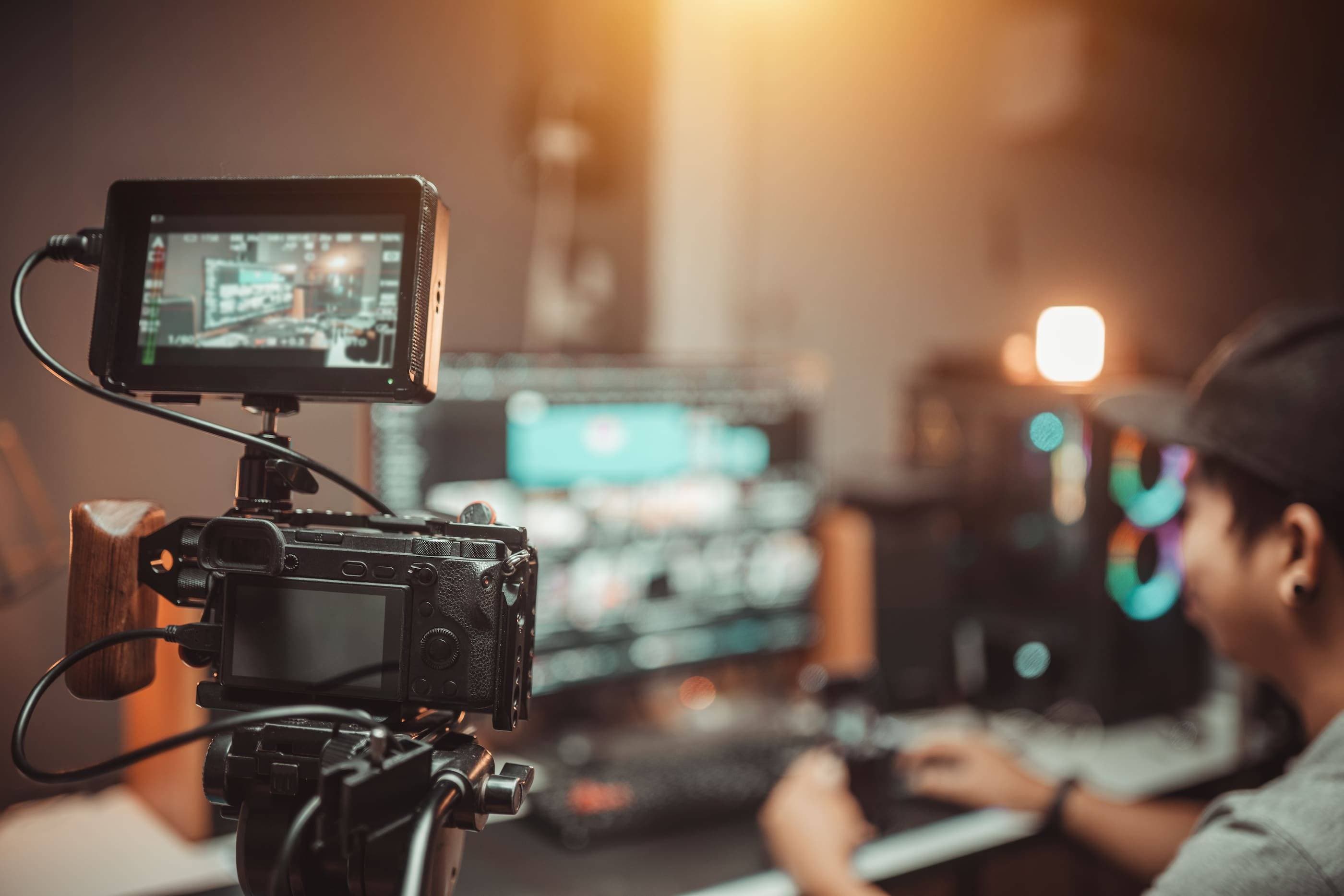 A man is using a video camera in front of a monitor.