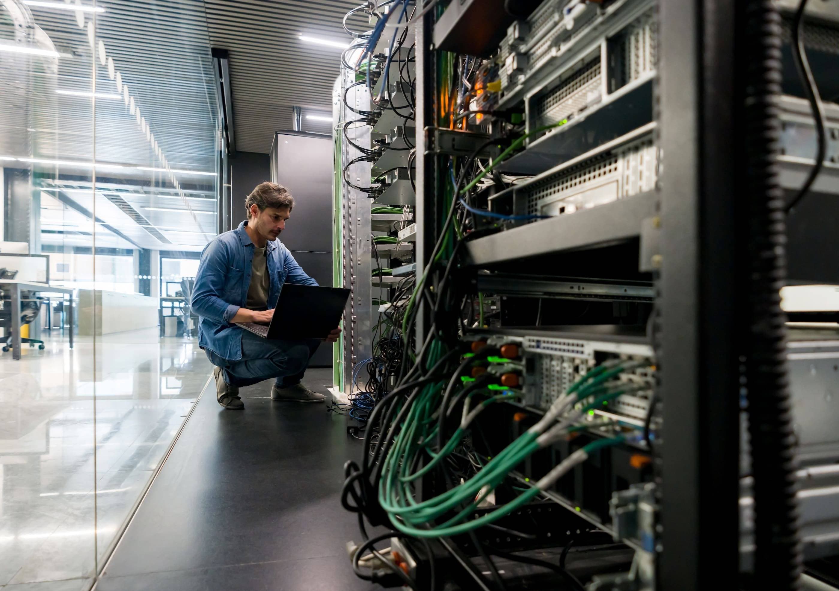 A man working on a laptop in a server room.