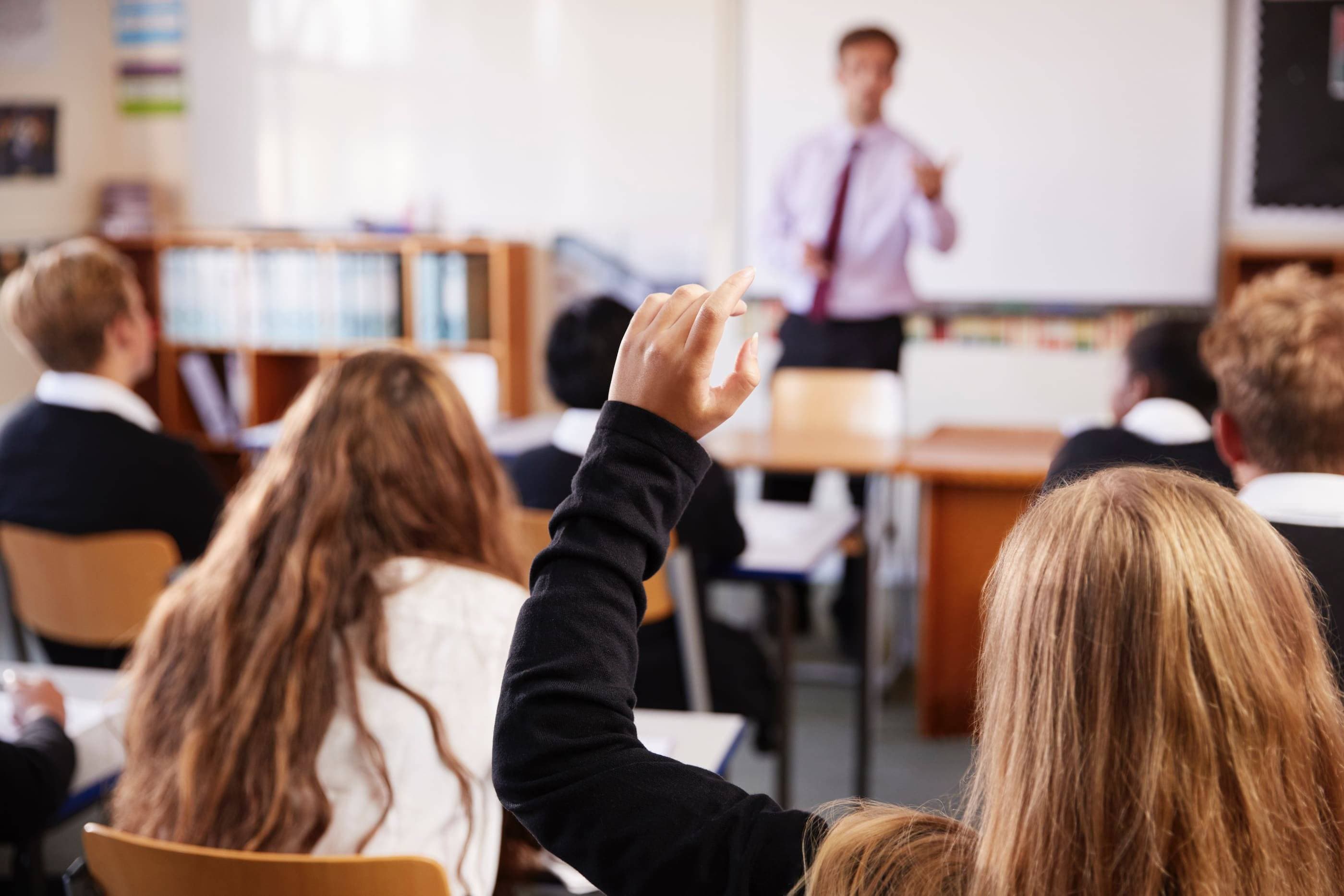 A group of students in a classroom raising their hands.