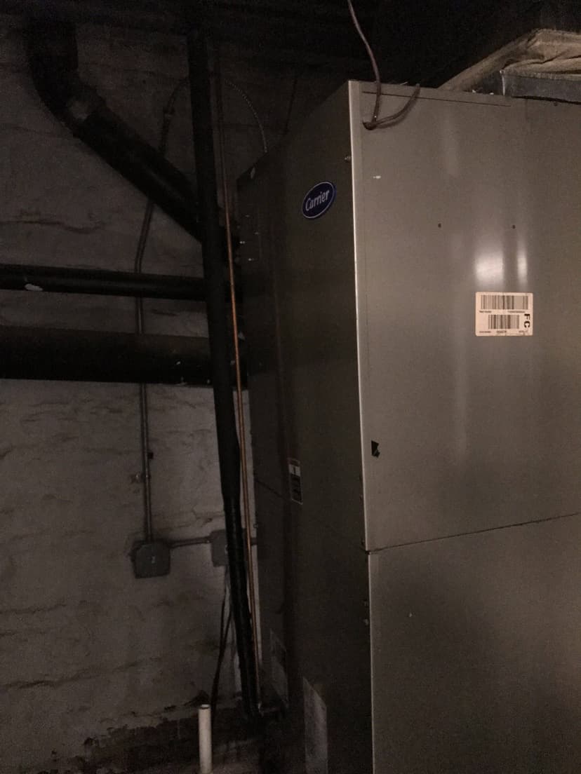 A metallic HVAC unit with a Carrier logo is installed against a brick wall in a dimly lit area, providing efficient interior cooling.