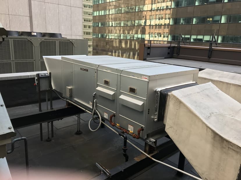 Large rooftop-mounted HVAC unit with ventilation ductwork and a makeup air unit on a building. Various pipes and wiring are also visible.