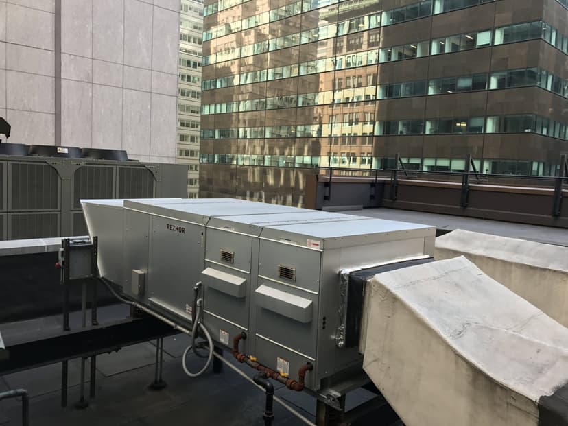 An array of commercial HVAC outdoor units on a rooftop, surrounded by modern office buildings.