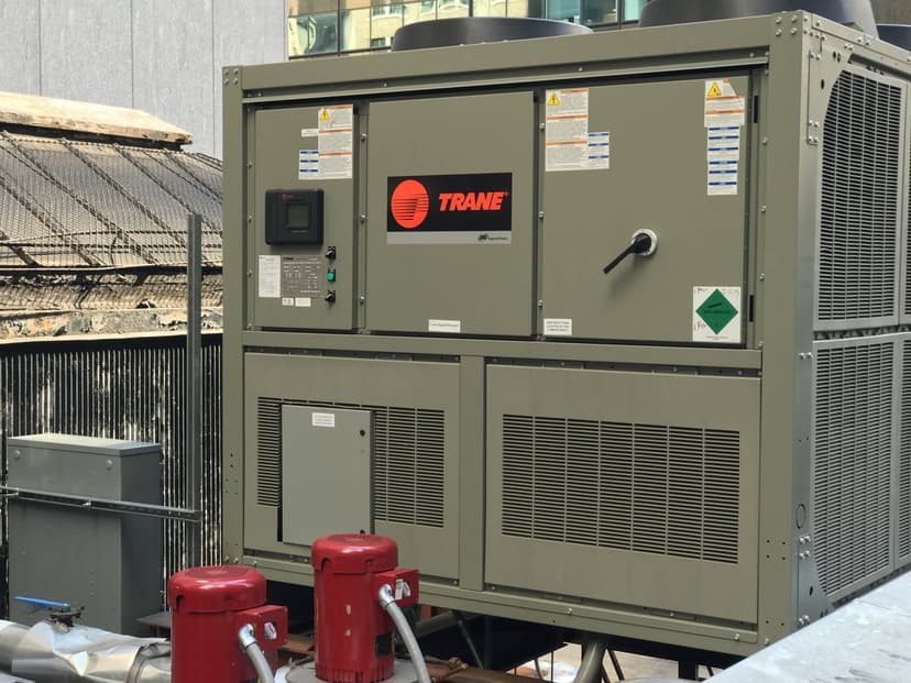 Commercial HVAC outdoor units by Trane, featuring a control panel and red pipelines, located in an urban building setting.