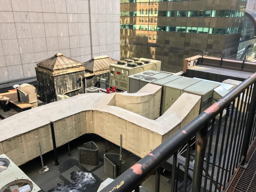 Rooftop view of an urban building featuring ventilation systems, air conditioning units, and commercial HVAC outdoor units amidst surrounding modern buildings.