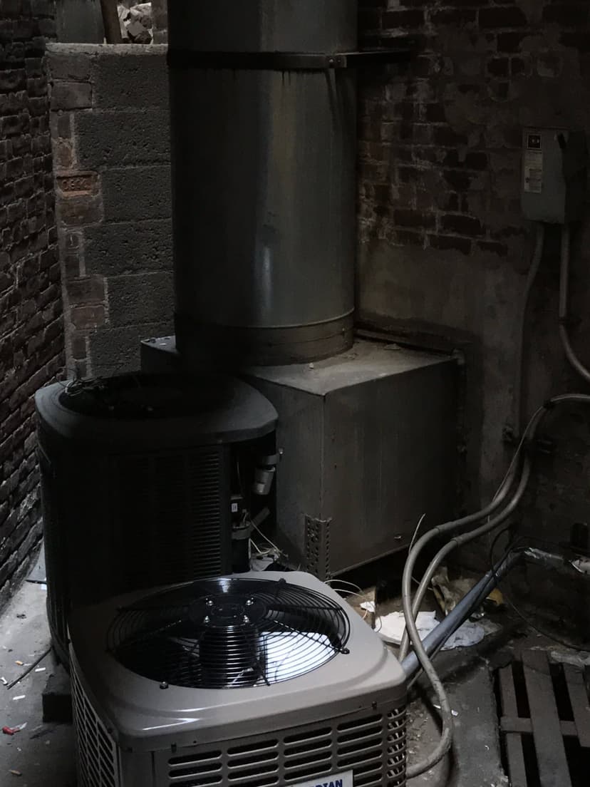 Two commercial HVAC outdoor units situated in a narrow alleyway between brick walls.