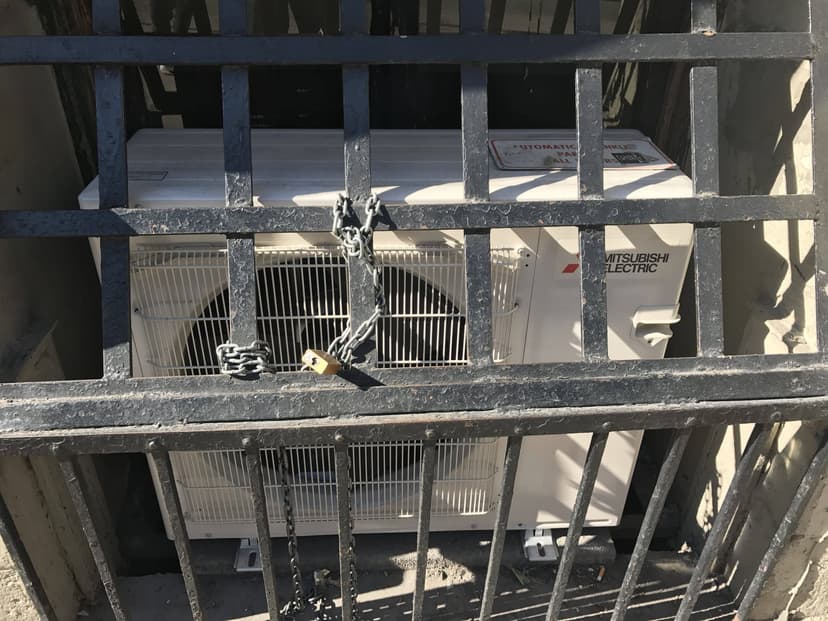 Commercial HVAC outdoor units behind a metal gate with a chain and lock securing them.