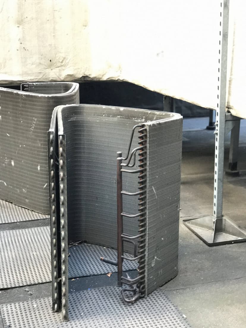 Curved structures made of layered material, possibly 3D printed, are set against a textured surface in an industrial setting near commercial HVAC outdoor units.