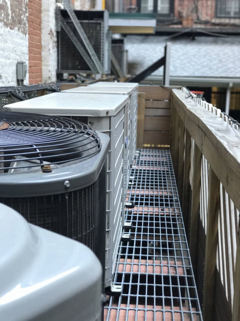 A narrow outdoor platform with commercial HVAC units and equipment lined up along a wooden fence.