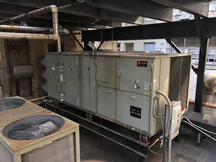 Industrial air handling and packaged unit HVAC systems on a building rooftop, surrounded by pipes and vents.