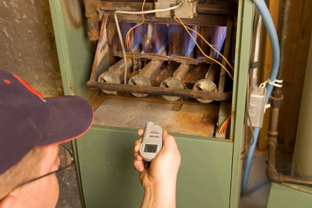 A man using a thermometer to check the temperature of a furnace.