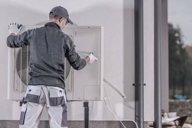 A man fixing an air conditioner on a wall.