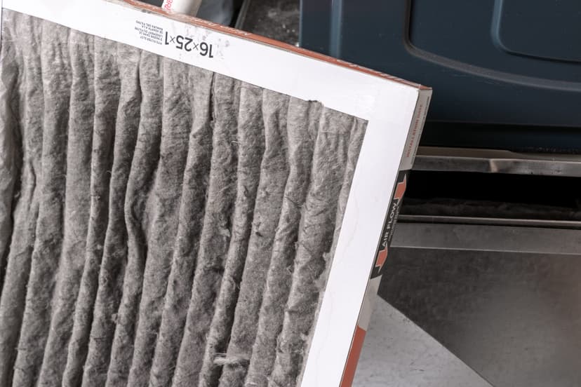 A used, dirty HVAC filter being removed from a blue HVAC unit.