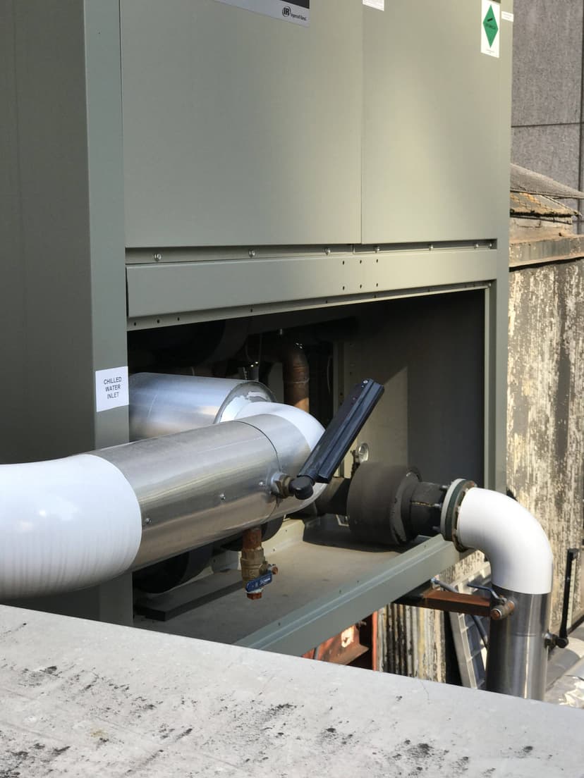 Outdoor industrial HVAC system with large pipes and a control panel; unit mounted on a building exterior, featuring chilled water leave return functionalities.